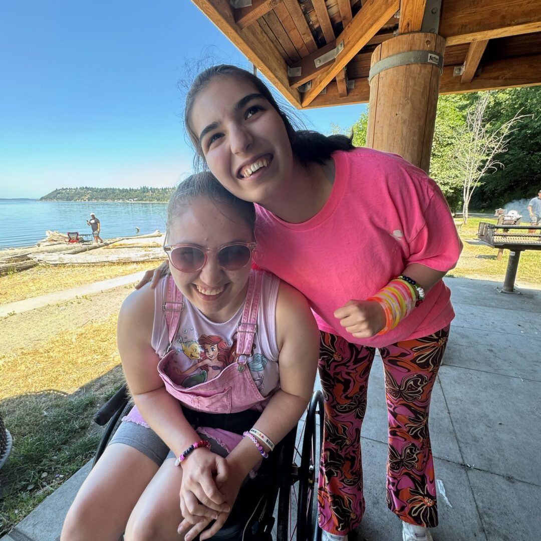 Two women posing for a picture in front of the water.